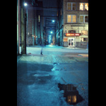Blurry time exposure of woman walking past alley along Vancouver's Hastings Street, wet pavement night shot