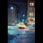 Blurry shot of yellow taxi pulling out of alley onto Vancouver's Hastings Street, wet pavement night shot